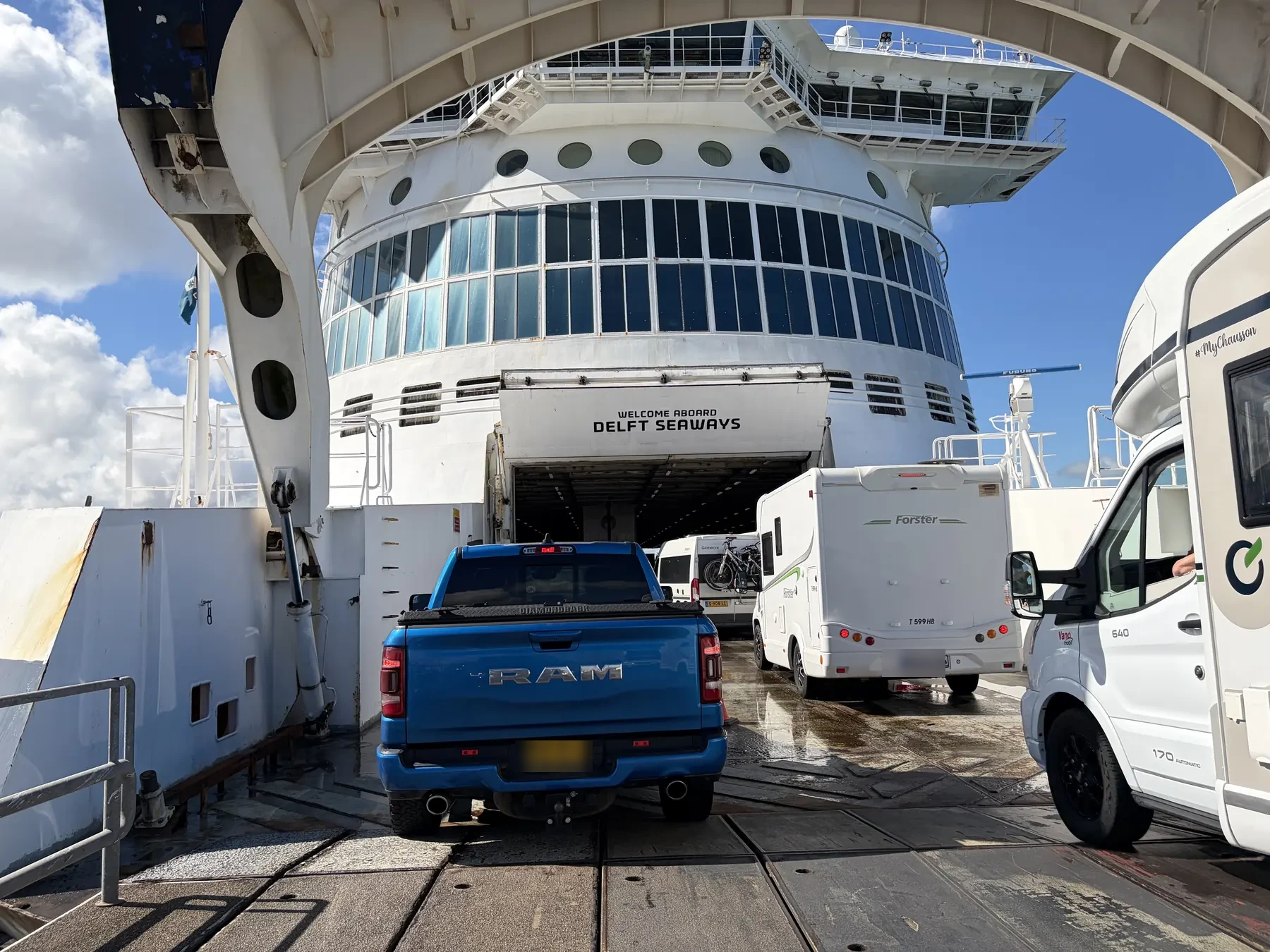 Wohnmobile und ein Pick-up fahren unter Welcome aboard Delft Seaways auf das Autodeck